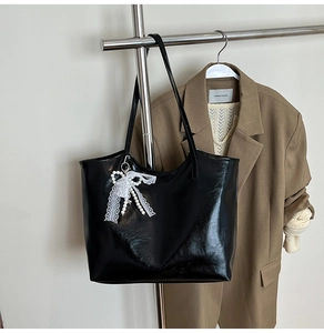 Dettaglio della borsa tote nera lucida con ciondolo in pizzo e perle sul gancio in metallo