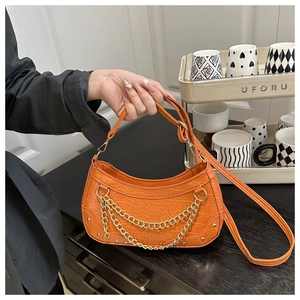 Detail of orange crocodile pattern crossbody bag with layered gold chains and studs