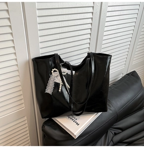 Dettaglio della borsa tote nera lucida con ciondolo a fiocco in pizzo e perle eleganti