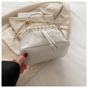 Detail of white lace and leather bucket bag with pearl handle and golden chain strap