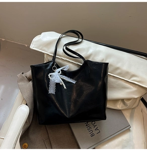 Dettaglio della borsa shopper nera lucida con fiocco in pizzo bianco e decoro di perle