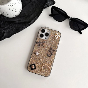 Close-up of golden glitter phone case featuring 3D bow, pearl, and rhinestone charms