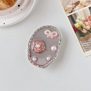 Détail du camélia rose et du nœud en perles sur un support de téléphone ovale chic