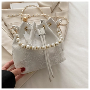 Detailed macro view of white lace floral embroidery on bucket bag with pearl handle