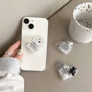 Macro view of heart-shaped glitter phone grip with bear and flower charms on white phone