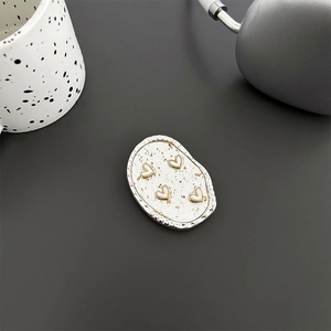 Detail of silver phone grip with gold foil and four pink white hearts on dark background