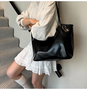 Grande borsa shopper nera lucida indossata da una modella in un ambiente minimalista