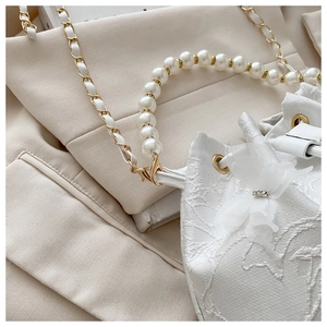 Detail of floral lace bucket bag featuring pearl handle and white leather chain strap