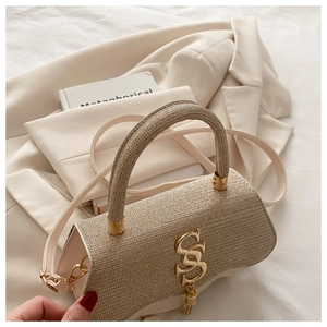 Détail du sac à main en tweed avec logo doré et pompon sur un blazer beige