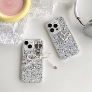 Sparkly silver glitter iPhone case featuring pearl bow and heart pendant on a yellow tray