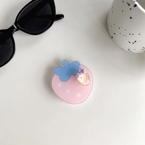 Close-up of cute pink strawberry rotating phone grip with mini pendant on white desk