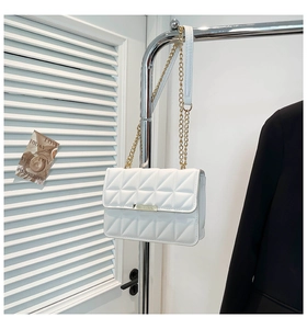 Detail of white quilted crossbody bag featuring a golden chain strap and buckle closure