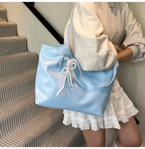 Dettaglio della borsa tote azzurra con bordo in pizzo bianco e ciondolo a fiocco di perle