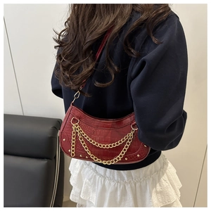 Detail of burgundy crocodile-textured crescent bag with layered gold chain and rivets