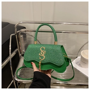 Détail du petit sac à main vert pailleté avec logo doré, gland à franges et bordure ondulée