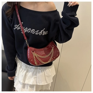 Detail of burgundy crescent bag with crocodile pattern and triple gold chains on model