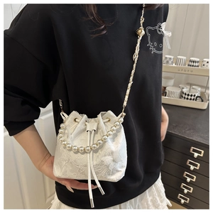 Close-up of white lace bucket bag with pearl handle and 3D butterfly ornaments
