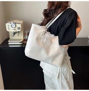 Close-up of white leather tote bag with lace bow and pearl pendant in a cozy cafe setting
