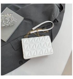 Detail of white quilted crossbody bag with gold chain strap on grey blazer