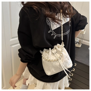 Detail of white lace bucket bag with large pearl handle and woven chain strap