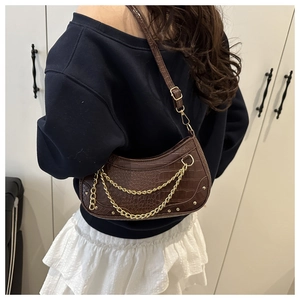 Detail of dark brown crocodile embossed baguette bag with double gold chains and rivets