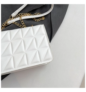 Macro shot of white quilted shoulder bag showing triangular patterns and gold chain strap