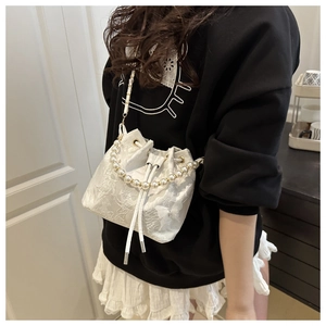 Detail of white embroidered bucket bag with pearl handle and floral lace textures