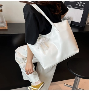 Detail view of large white tote bag featuring a lace bow and pearl charm on shiny leather