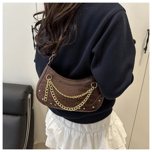 Detail of dark brown faux crocodile leather bag with gold chains and studs on a model