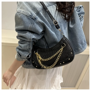 Detail of black croc-effect underarm bag with gold double chains and rivets on shoulder strap