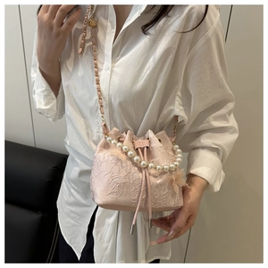 Detail of pink lace bucket bag with pearl handle and embroidery on white shirt