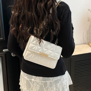 White quilted crossbody bag with gold chain strap shown on model in modern interior
