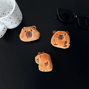 Close-up of three plush capybara phone grips featuring detailed embroidery on black surface
