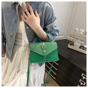 Detailed view of a green leather handbag with a pink flap and gold buckle on a model