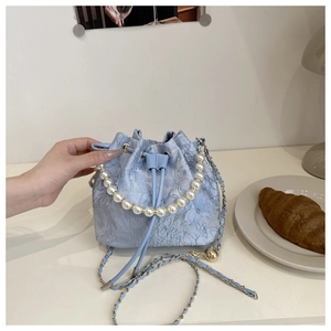 Close-up of light blue lace bucket bag with pearl handle and golden chain strap