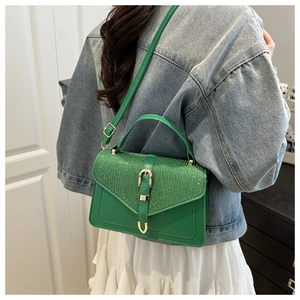 Close-up of green sequined crossbody bag with golden horseshoe buckle on a female model