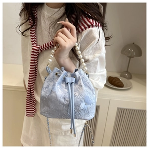 Detail of light blue bucket bag featuring floral lace embroidery and pearl handle accent