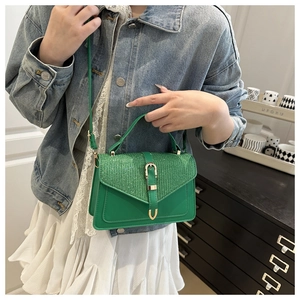 Detail of forest green crossbody bag with sequin flap texture and golden horseshoe buckle