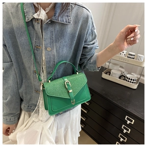 Close-up of green leather handbag with glittery woven texture and golden metal buckle