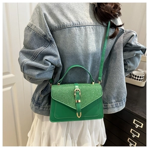 Detail of green shoulder bag with V-shaped glitter panel and gold buckle in lifestyle setting