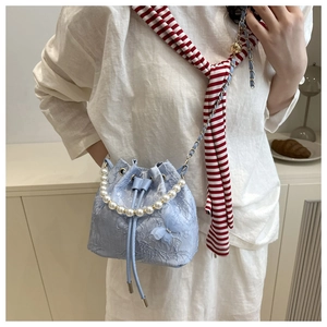 Détail du sac seau en dentelle bleu clair avec poignée en perles et nœud en soie