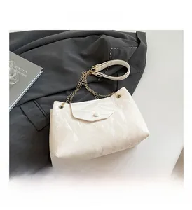 Detail der cremefarbenen Tasche mit goldener Kette und glänzender Plissee-Struktur