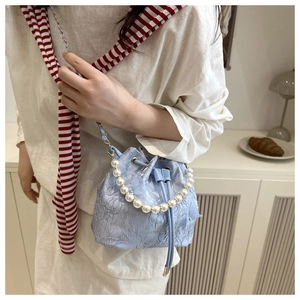 Close-up of light blue lace bucket bag with large pearl handle and metal chain strap