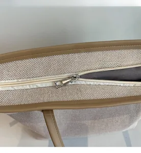 Close-up of smooth metal zipper and brown leather trim on the white canvas tote bag