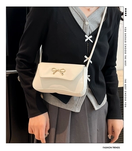 Detail of white leather baguette bag featuring a gold bow accent and thin shoulder strap