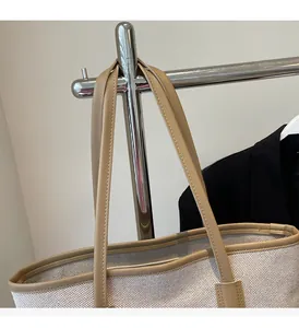 Detail view of woven canvas tote bag with brown leather handles and reinforced stitching