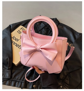 Close-up of pink bucket bag featuring a large decorative bow and elegant metal ring handle