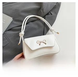 Close-up of white leather baguette bag featuring a gold bow accent and knotted cord strap