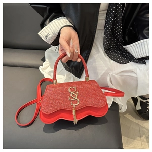 Détail d'un sac à main rouge pailleté avec logo SS doré et bord inférieur ondulé