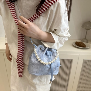 Pale blue bucket bag with floral lace embroidery and pearl handle worn by model